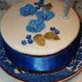 A simple cake decorated with blue and gold sugar crafted flowers and leaves.