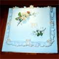 A 70th birthday cake.  A square rich fruit cake with sugar crafted floral decoration, frills and bows.