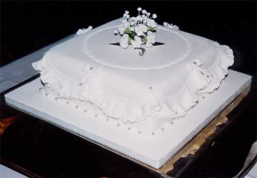 Square cake with spray of white sugar crafted flowers for a Silver Wedding celebration.
