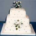 A three-tiered, stacked fruit and sponge wedding cake decorated with blue and ivory roses.