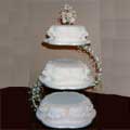 Modern petal-shape 3-tier wedding cake with cream, peach and white sugar crafted flowers on top tier.  There are peach sugar crafted bows on each tier.